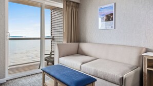 A room with a beige sofa, a blue bench, a wooden side table, a framed picture on the wall, and a view of the water through a sliding door. - Alexandra Inn (Traverse City)