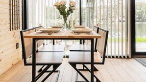 A modern dining area with a wooden table and chairs, large windows with blinds, and a view of the outdoors. - Lakefront cabin #5 / Leisure Lake Resort (Pocono Township)