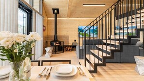 A modern interior with a wooden floor, a fireplace, a staircase with black railings, and a dining area with a vase of flowers. - Lakefront cabin #5 / Leisure Lake Resort (Pocono Township)