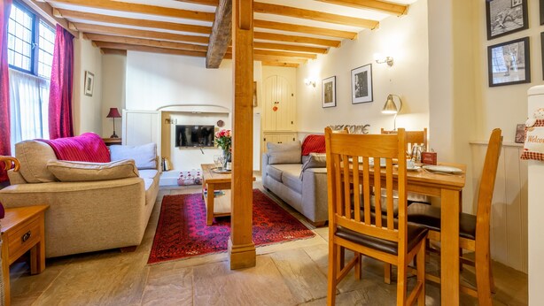 A cozy living room with a sofa, a dining table with chairs, a kitchen area, and a wooden ceiling structure. - The Dutch House -  a family break that sleeps 4 guests  in 2 bedrooms (York)