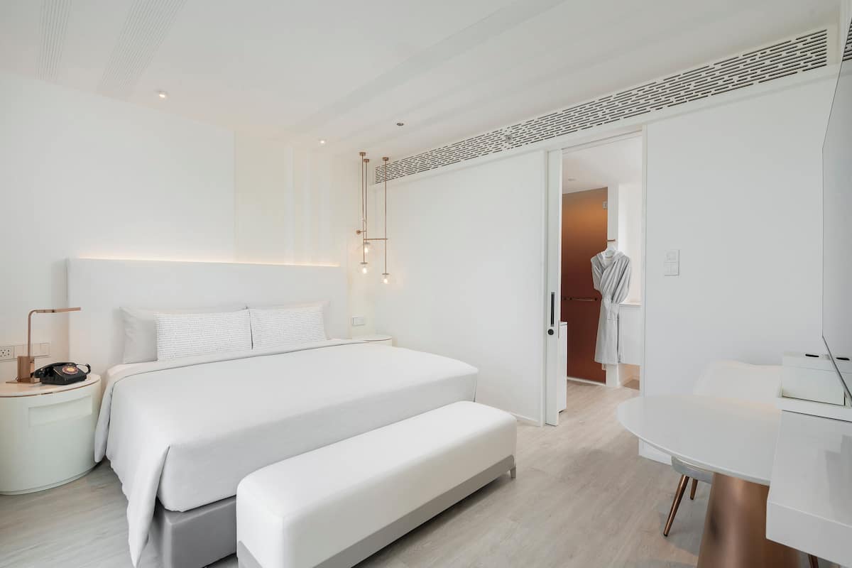 A modern bedroom with a large bed, bedside tables, a desk, and a walk-in closet.