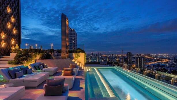 A rooftop pool area with lounge seating and a cityscape view.