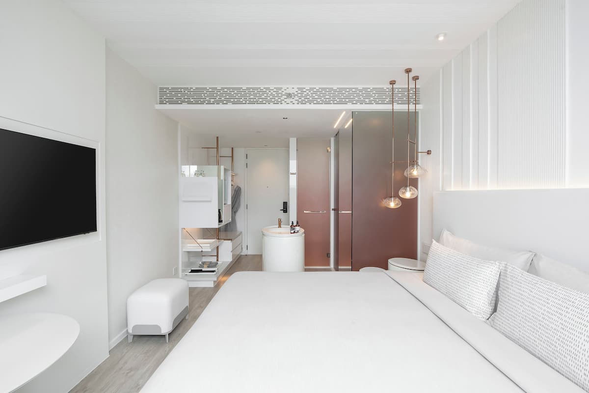 A modern bedroom with a large bed, bedside tables, a TV, and a bathroom in the background.