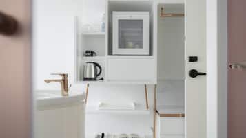 A modern bathroom with a white sink, a kettle, and a small shelf with toiletries.