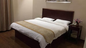 A neatly made bed with a wooden headboard, a bedside table with a vase of flowers, and a painting on the wall. - Greentree Inn Wuxi New District High Speed Rail Station Newland Family Express Hotel (Wuxi)