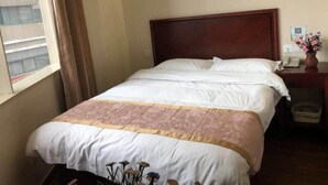 A hotel room with a bed, a nightstand with a phone and a vase of flowers, and a painting on the wall. - Greentree Inn Wuxi New District High Speed Rail Station Newland Family Express Hotel (Wuxi)