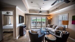 Ein Hotelzimmer mit Balkon, einer Couch, einem Couchtisch und einem Fernseher.
