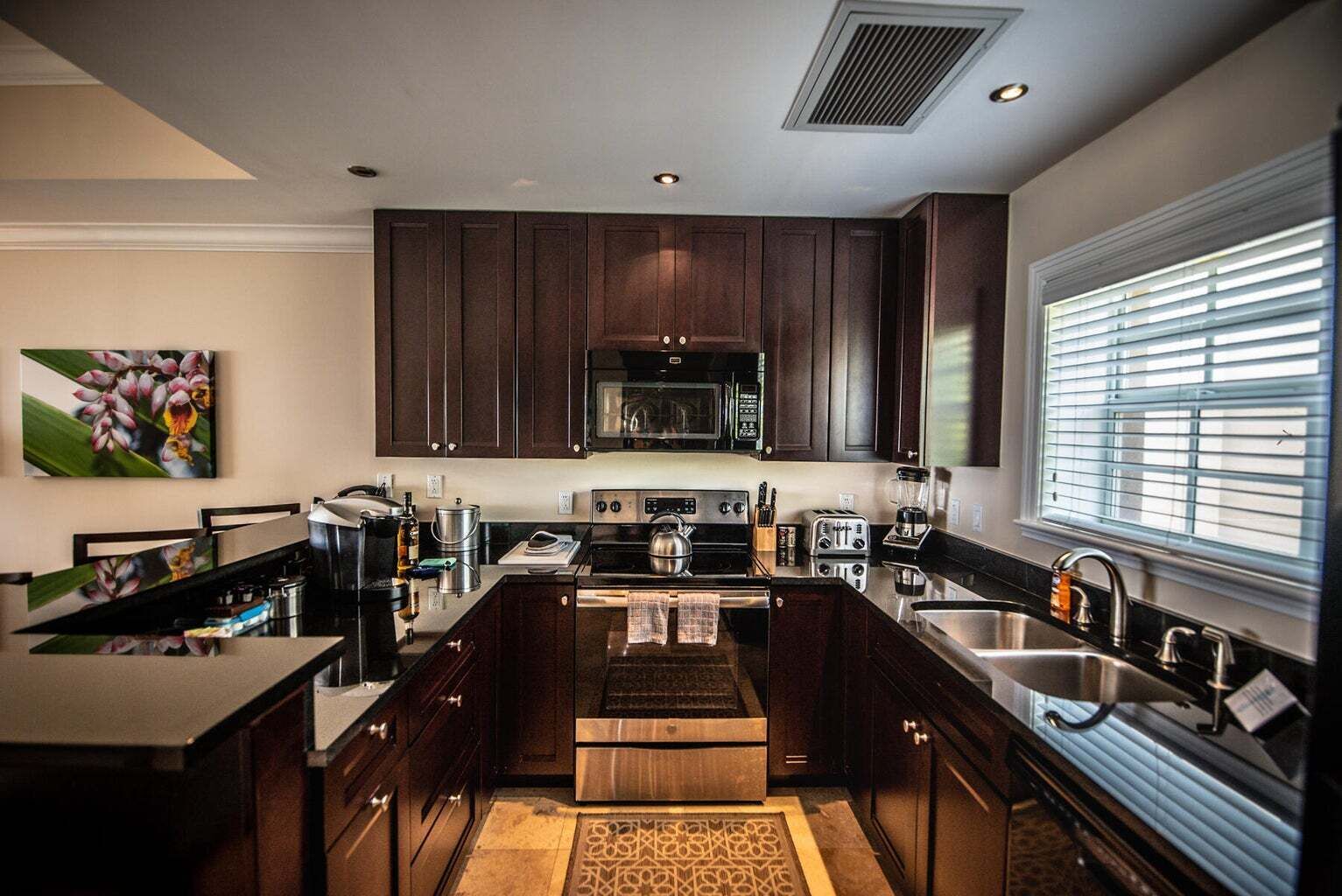 A modern kitchen with dark wood cabinets, stainless steel appliances, and a large window with blinds.