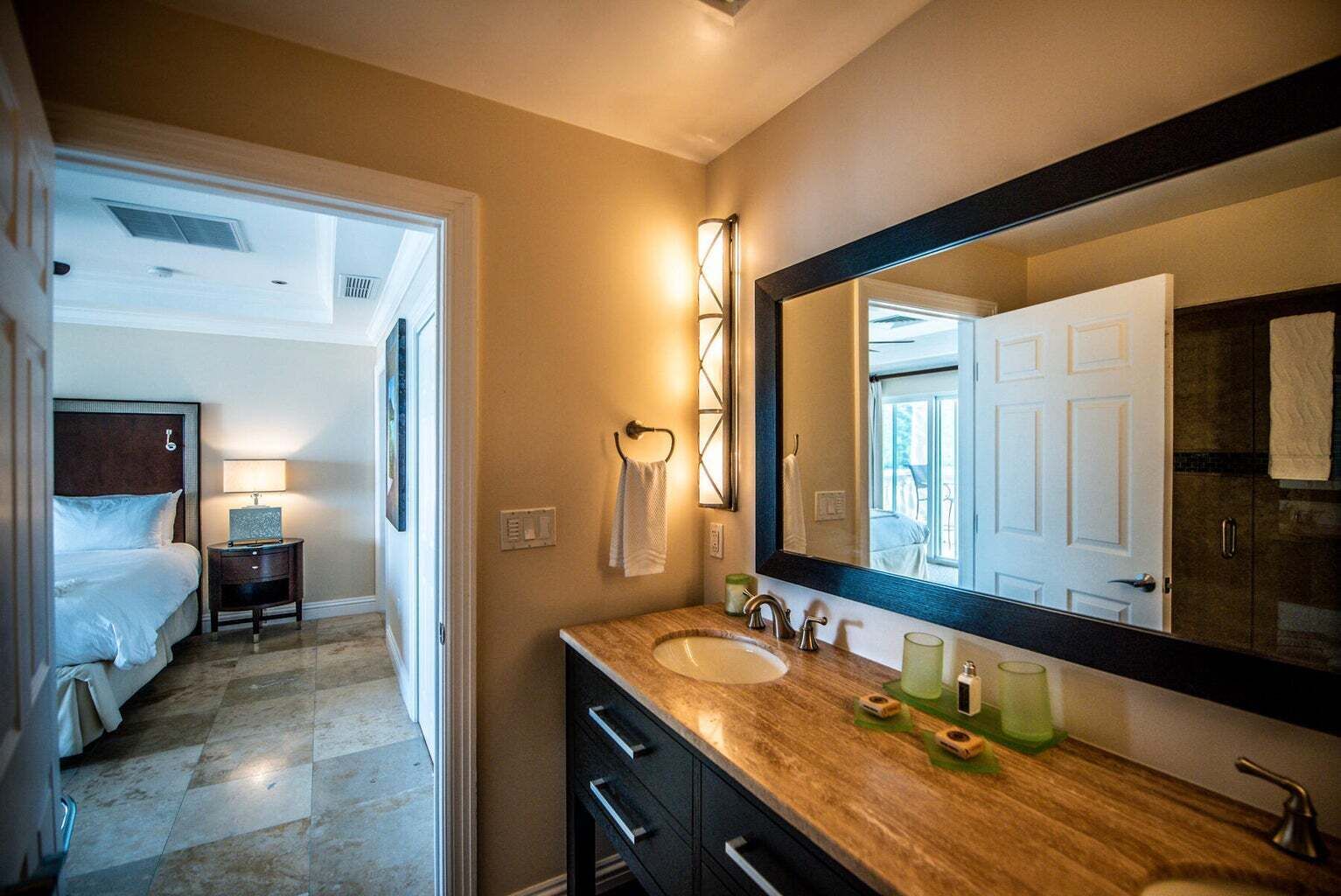 A hotel bathroom with a large mirror, two sinks, and a vanity with drawers.