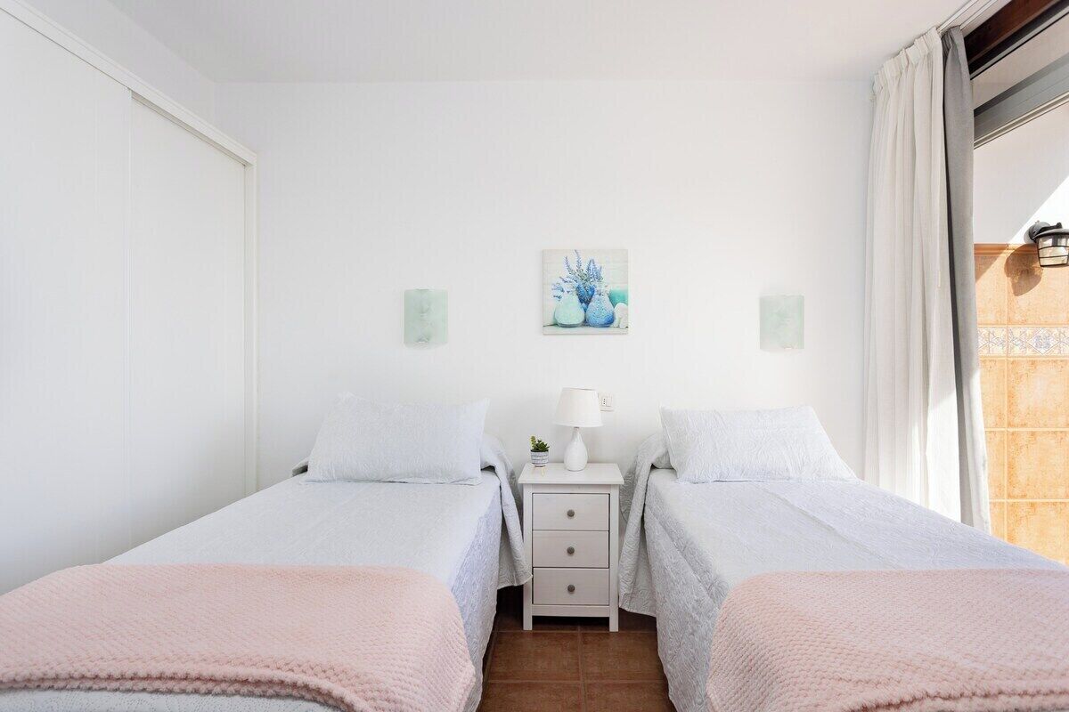 Un dormitorio con dos camas individuales, una mesita de noche con lámpara y un cuadro en la pared.