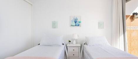 Un dormitorio con dos camas individuales, una mesita de noche con lámpara y un cuadro en la pared.