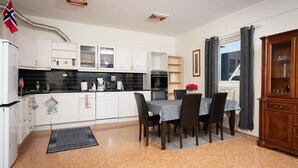 Een kleine keuken met witte kastjes, een eettafel met stoelen, een houten kast en een vlag.