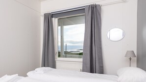 Een hotelkamer met een bed, een raam met grijze gordijnen, een ronde wandklok en een lamp.