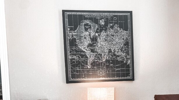 Een kamer met twee houten stoelen, een ronde metalen tafel, een lamp en een wereldkaart aan de muur.