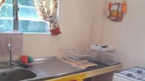 Une cuisine avec des meubles de couleur jaune, une cuisinière à gaz et une fenêtre avec des rideaux.