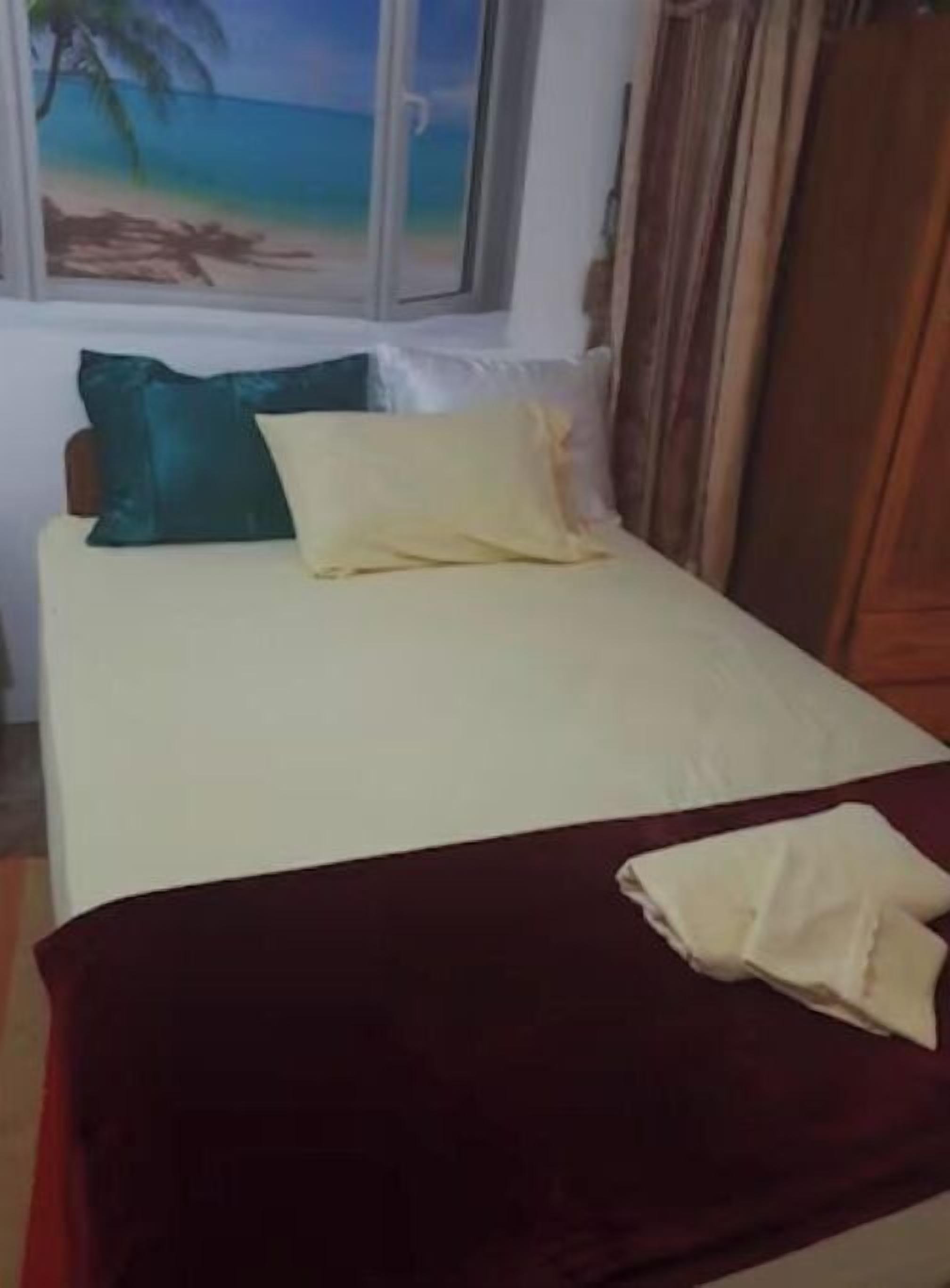 Un lit avec un drap blanc et une couverture rouge, un oreiller turquoise et un oreiller jaune.