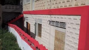 Un bâtiment à la façade rouge et blanche, avec un escalier menant à l’entrée et une porte dotée d’une grille métallique.