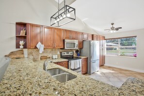 A kitchen with granite countertops, wooden cabinets, stainless steel appliances, and a window with blinds.