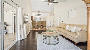 Un salon spacieux avec un canapé beige, une table basse en verre et un ventilateur de plafond.