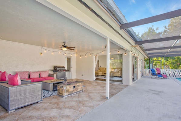 An outdoor patio with a covered seating area, a grill, and a pool in the background.