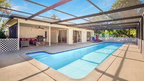 Une piscine couverte avec une structure en verre, un espace patio aménagé avec des sièges et une vue sur l’extérieur.