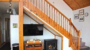 A living room with a wooden staircase, a television, a fireplace, and a small cabinet.