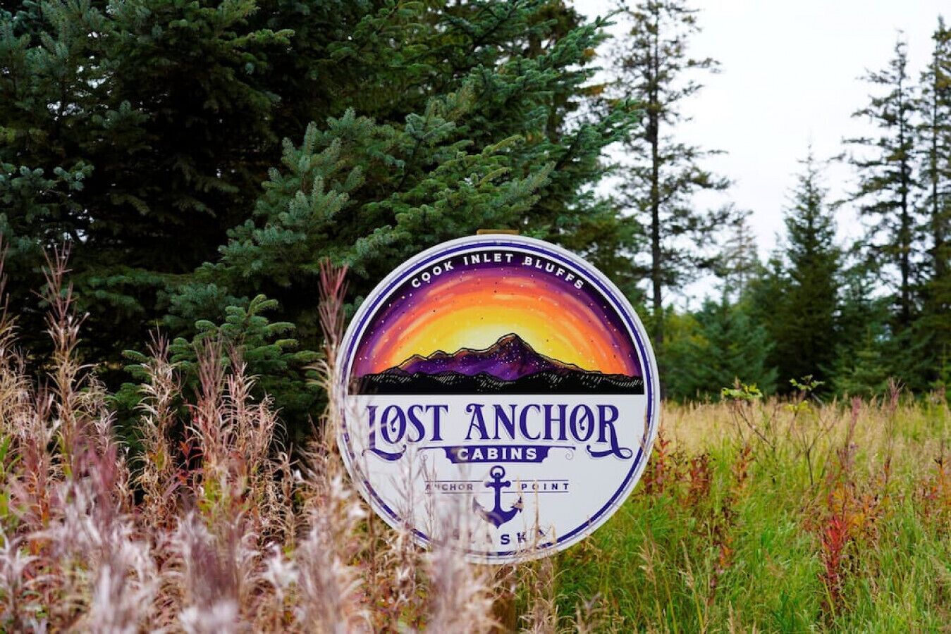 Une enseigne pour les cabanes « Lost Anchor », avec une illustration représentant un coucher de soleil et des montagnes.
