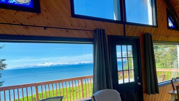 A room with a wooden interior, a view of the ocean, a door with curtains, and a chair with a blanket.