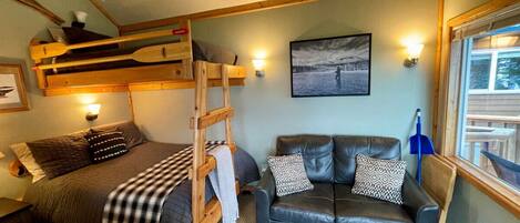 A cozy room with a bunk bed, a sofa, a wooden ladder, and a painting on the wall.
