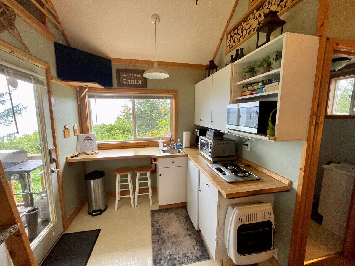 A compact kitchen with a window, a microwave, a sink, and a small refrigerator.