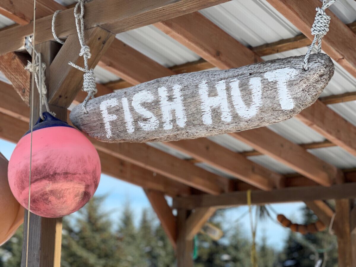 Une pancarte en bois portant l’inscription « CABANE À POISSON » est suspendue à une structure.