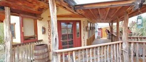 A rustic wooden building with a porch, a barrel, and signs reading "TAQUERIA" and "CERVEZA".
