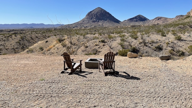 Un paysage désertique avec deux chaises en bois et une table en béton, le tout installé sous une structure en bois.