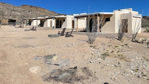 Un bâtiment de style désertique comprenant plusieurs pièces, des espaces de repos en plein air et une végétation clairsemée.
