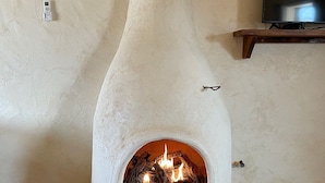 Une cheminée en pierre avec un feu qui crépite à l’intérieur, un climatiseur fixé au mur et un téléviseur posé sur une étagère en bois.