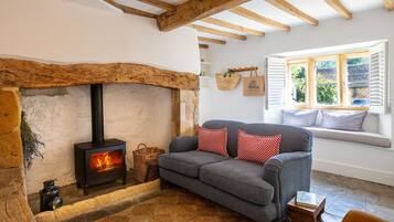 A cozy living room with a stone fireplace, a grey sofa, and a window with white shutters.