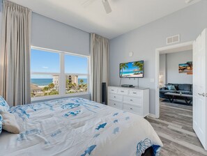 A bedroom with a large bed, a TV, and a view of the ocean.