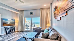 A modern living room with a sofa, armchairs, a coffee table, and a TV. There is a balcony with a view of the ocean and a dining area with chairs and a table. - Madeira Bay 1502- Bayside with Stunning Gulf Views! (Madeira Beach)