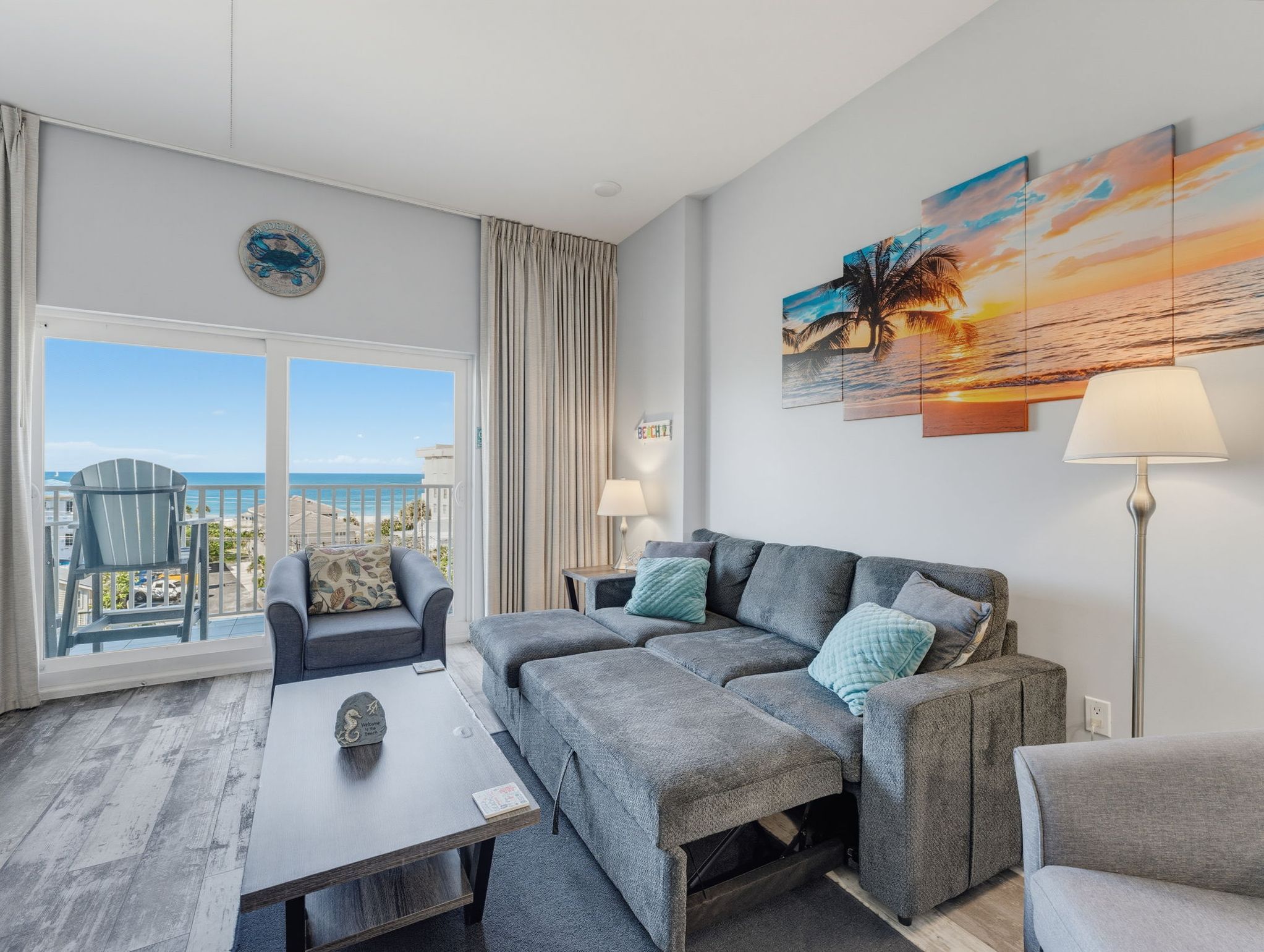 Un salon moderne avec un canapé, un fauteuil et une vue sur la mer grâce à de grandes fenêtres.