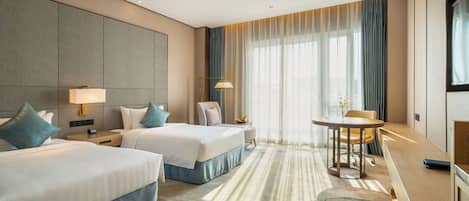 A hotel room with two beds, a desk, a chair, and a large window with curtains.