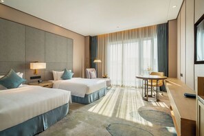 Habitación de hotel con dos camas, un escritorio, una silla, una mesa redonda y un ventanal grande con cortinas.