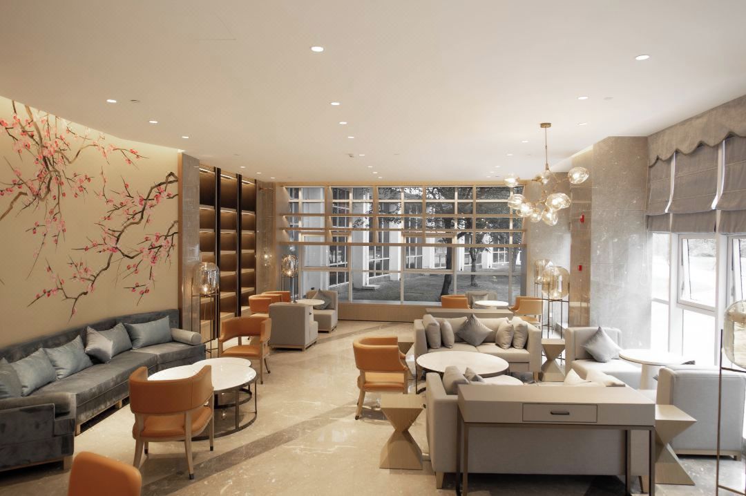 A modern lounge area with sofas, chairs, and a coffee table, featuring a large window and a decorative wall mural.