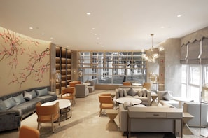 Un espacio lounge moderno con sofás, sillas y una mesa de centro, que cuenta con un gran ventanal y un mural decorativo.