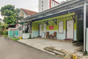 A building with a green and white facade, a red sign with contact numbers, and a set of wooden chairs outside.