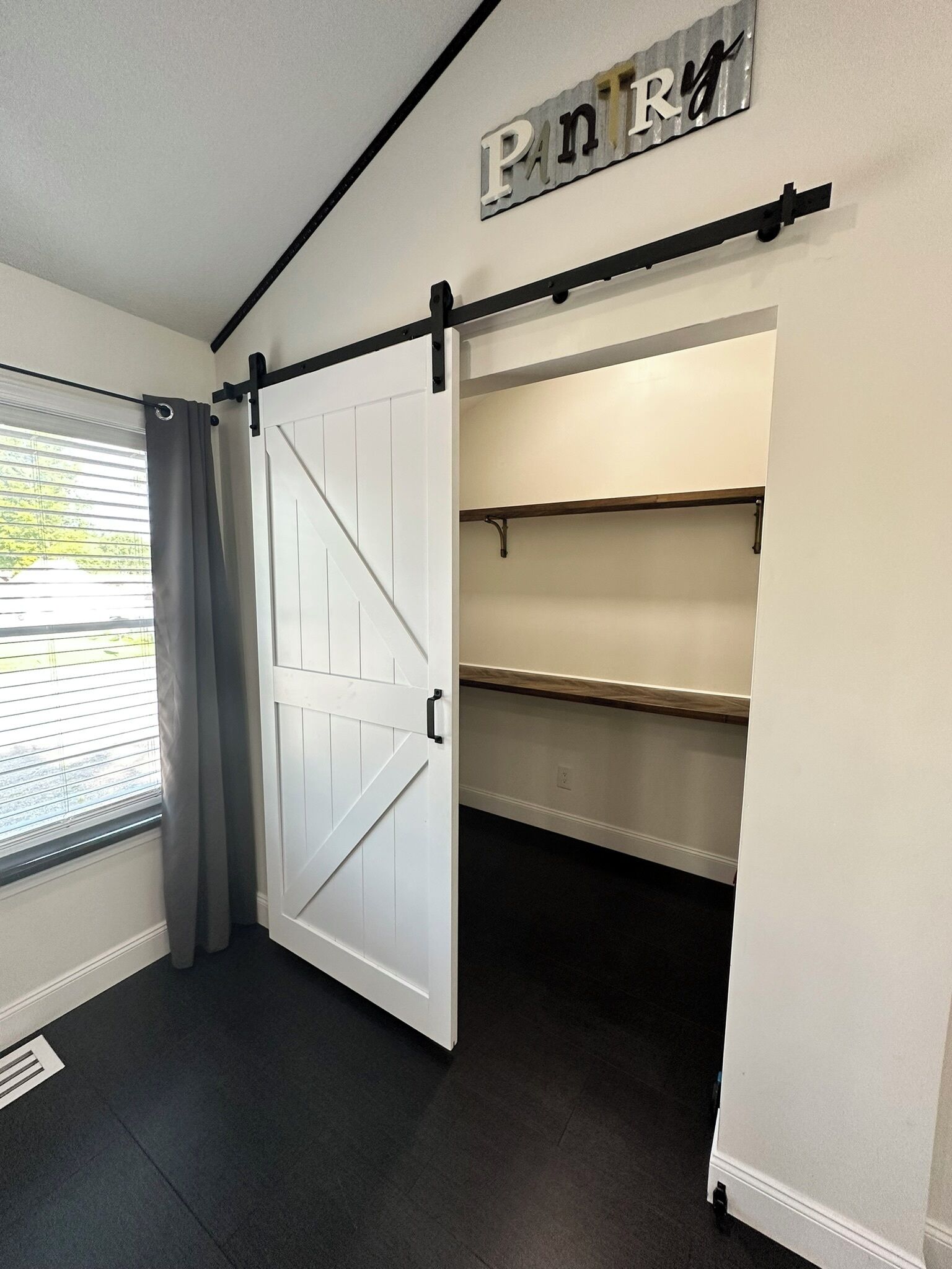 Una habitación con una puerta corrediza de estilo rústico, una ventana con persianas y un letrero sobre la puerta.