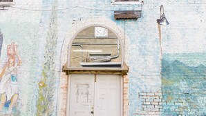 Un edificio desgastado por el tiempo con una puerta blanca, dos ventanas y un mural.