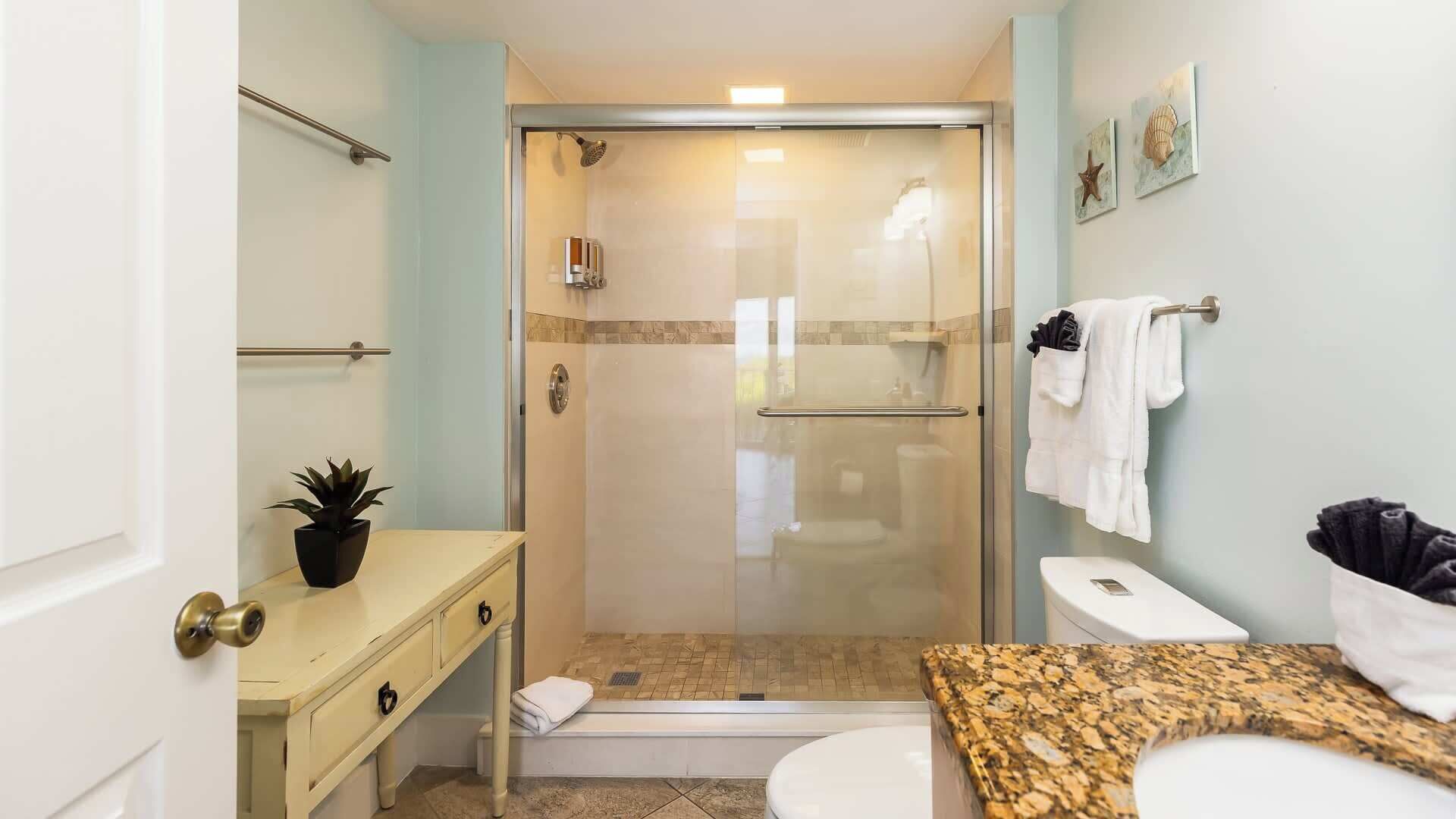 A bathroom with a glass-enclosed shower, a white toilet, a sink with a granite countertop, and a towel rack with towels.