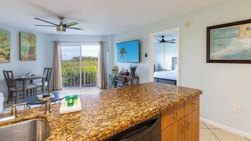 A kitchen with granite countertops, a dining area with a table and chairs, a balcony with a view, and a bedroom visible through an open door.