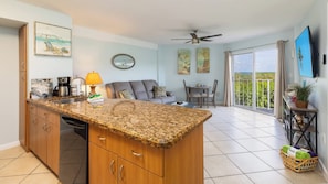 A modern kitchen with granite countertops, a dining area with a table and chairs, a sofa, and a balcony with a view. - Reel Key Largo Escape Ocean Pointe 5209 (Tavernier)