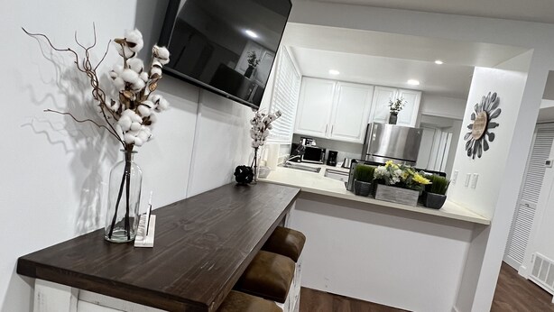 Una cocina moderna con armarios blancos, una encimera de madera oscura y un televisor de pantalla plana sobre la isla.